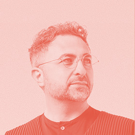 A man with short curly hair, a beard, and glasses looks slightly to the side. He is wearing a dark top and the image has a pinkish-red monochrome filter.